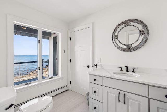 bathroom with toilet, a baseboard heating unit, a water view, wood finished floors, and vanity