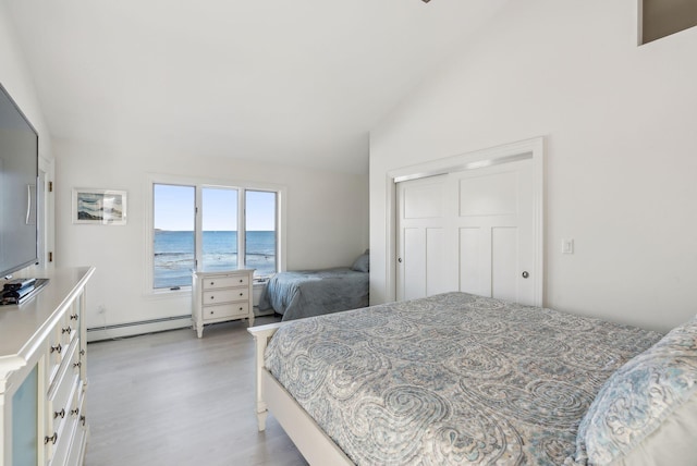 bedroom with lofted ceiling, a baseboard radiator, a water view, a closet, and light wood-type flooring