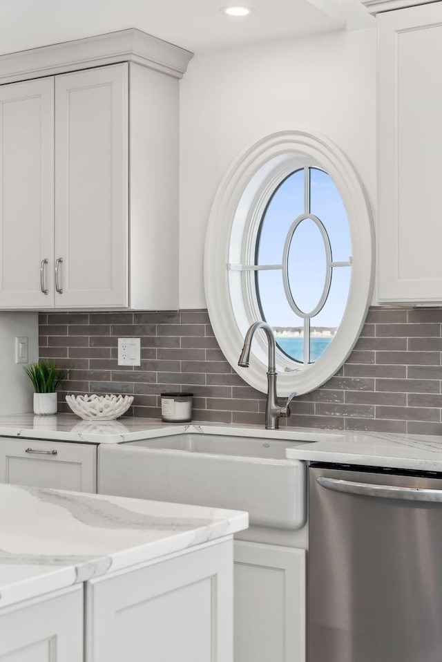 kitchen with a sink, white cabinetry, stainless steel dishwasher, decorative backsplash, and light stone countertops