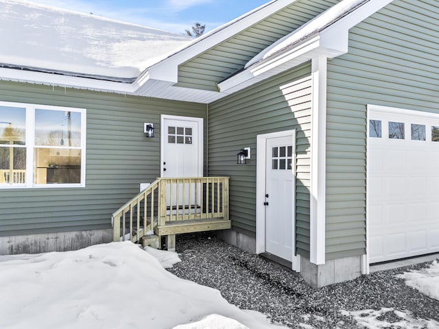 snow covered property entrance featuring an attached garage