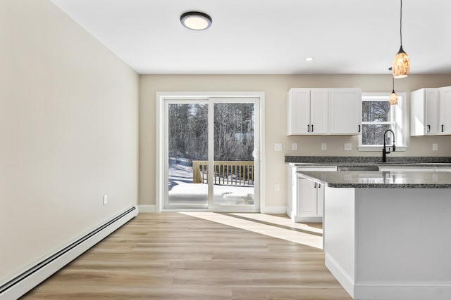 kitchen with white cabinetry, baseboard heating, light wood finished floors, dark stone countertops, and pendant lighting