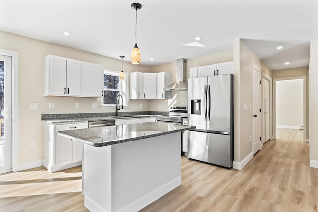 kitchen featuring white cabinets, appliances with stainless steel finishes, light wood-type flooring, wall chimney range hood, and a sink