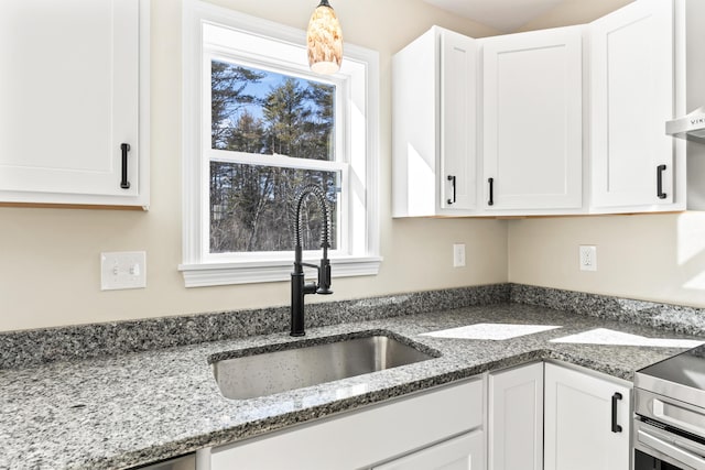 kitchen with a healthy amount of sunlight, white cabinets, a sink, and hanging light fixtures