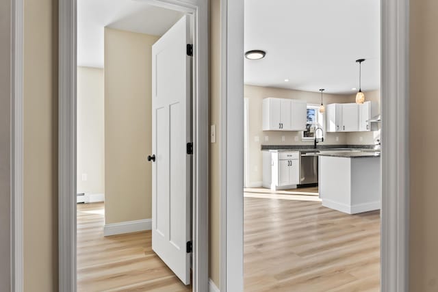 hall with light wood-type flooring, a sink, a baseboard radiator, and baseboards