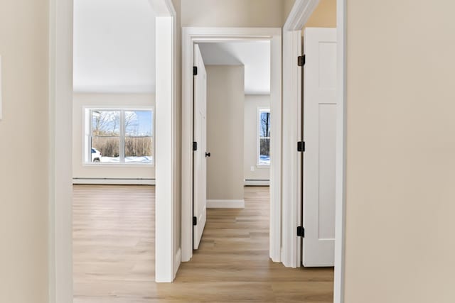 hall with a baseboard heating unit, light wood-type flooring, baseboards, and baseboard heating