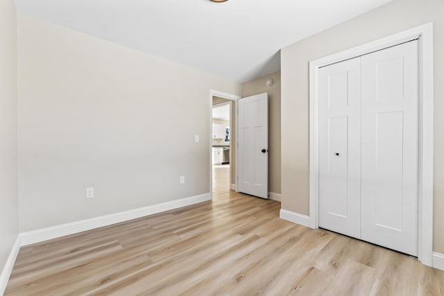 unfurnished bedroom featuring light wood-style flooring, baseboards, and a closet