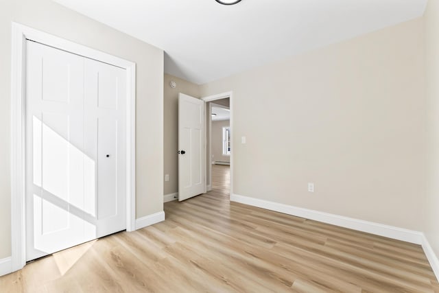 unfurnished bedroom with baseboard heating, a closet, light wood-type flooring, and baseboards