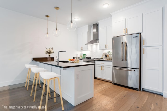 kitchen featuring high end refrigerator, dark countertops, wall chimney exhaust hood, a breakfast bar, and backsplash