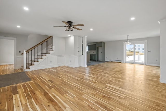 unfurnished living room featuring stairs, baseboard heating, recessed lighting, light wood-style flooring, and ceiling fan with notable chandelier