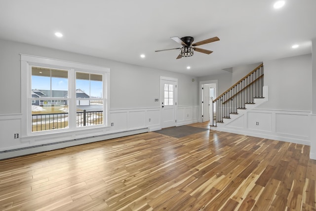 unfurnished living room with wood finished floors, a baseboard radiator, recessed lighting, ceiling fan, and stairs