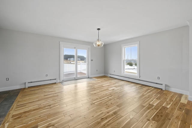 empty room featuring a wealth of natural light, light wood finished floors, and baseboard heating