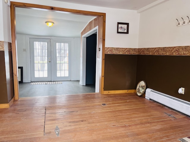 empty room with a baseboard radiator, wood-type flooring, and french doors