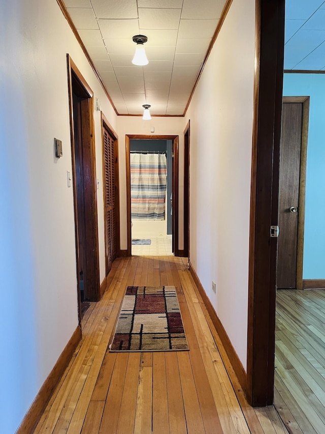 corridor with light wood-style floors, crown molding, and baseboards