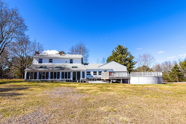 rear view of house with a sunroom, a lawn, roof with shingles, a chimney, and a deck