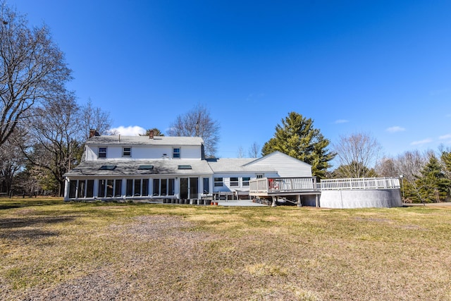 back of house featuring a wooden deck, a sunroom, a lawn, and a chimney