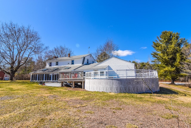 rear view of house featuring a shingled roof, a deck, a sunroom, a yard, and a chimney