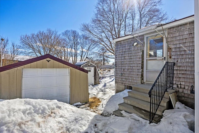 snow covered property with entry steps, a garage, and an outbuilding