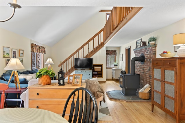 living area featuring a wood stove, high vaulted ceiling, wood-type flooring, and stairway