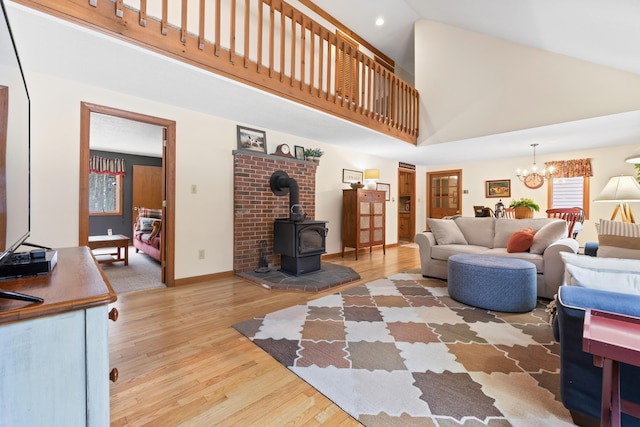 living area featuring a notable chandelier, a wood stove, wood finished floors, high vaulted ceiling, and baseboards