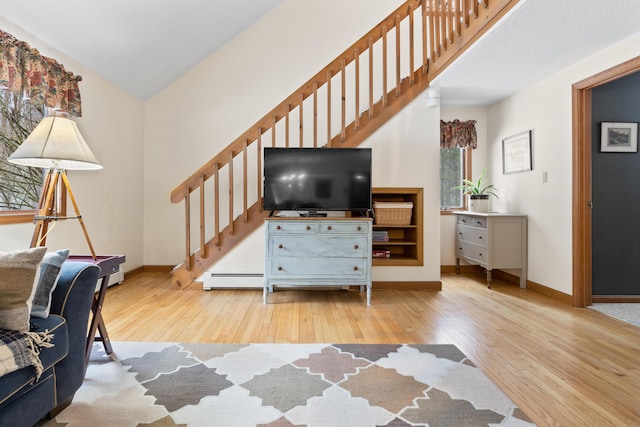 living area featuring a baseboard heating unit, stairway, wood finished floors, and baseboards