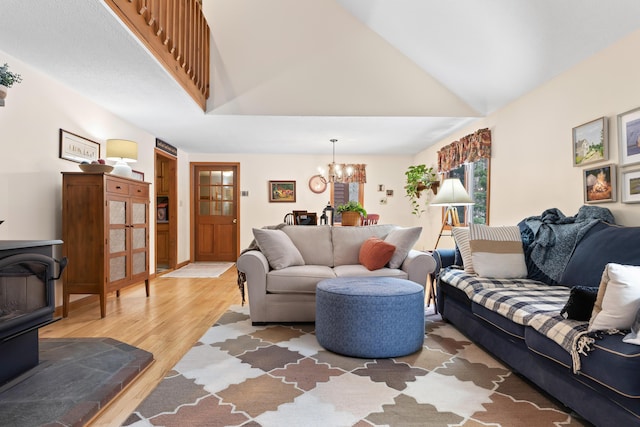 living area with a wood stove, an inviting chandelier, high vaulted ceiling, and light wood finished floors