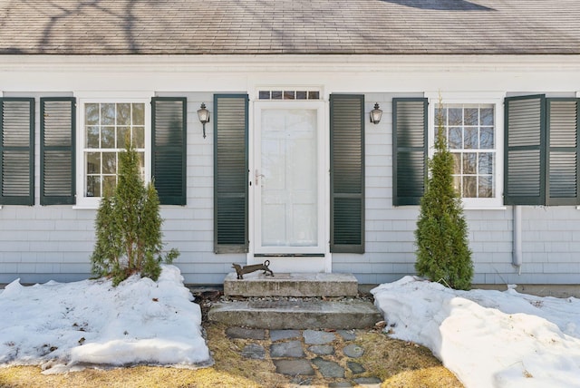 snow covered property entrance with a shingled roof