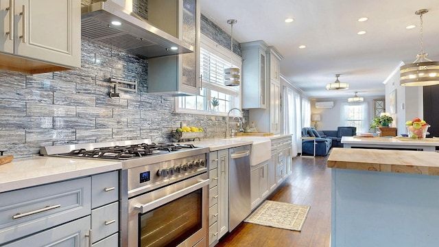 kitchen with dark wood-type flooring, gray cabinetry, open floor plan, appliances with stainless steel finishes, and wall chimney exhaust hood