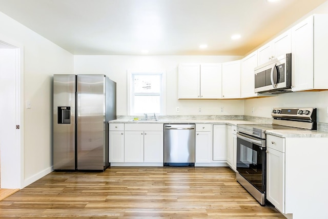 kitchen with light wood finished floors, white cabinets, appliances with stainless steel finishes, light countertops, and a sink