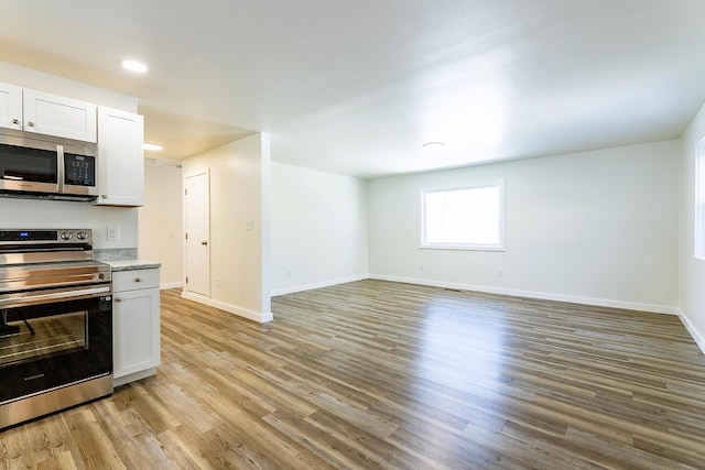 kitchen featuring light countertops, light wood-style flooring, appliances with stainless steel finishes, white cabinets, and baseboards