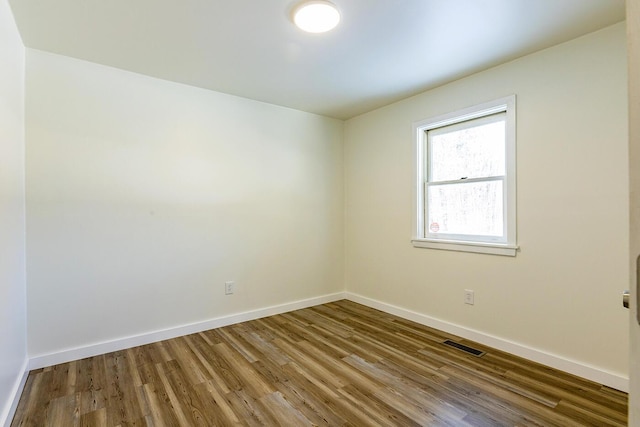 unfurnished room with baseboards, visible vents, and wood finished floors