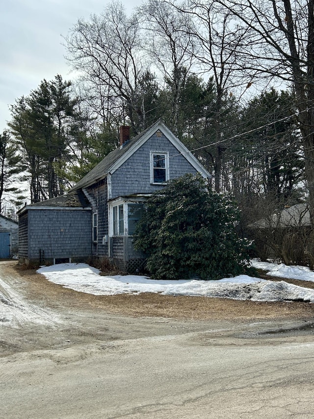 snow covered property featuring dirt driveway and a chimney