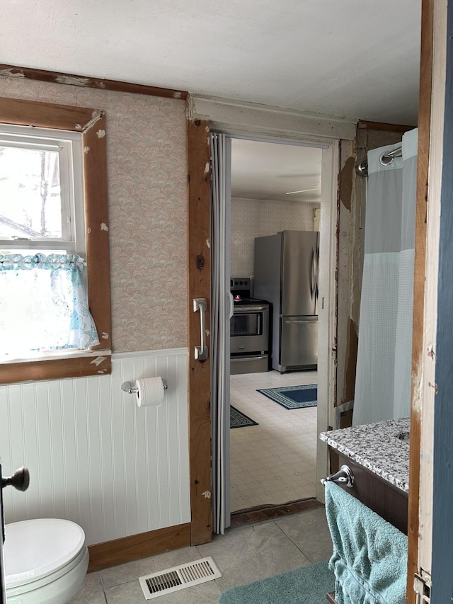 bathroom featuring vanity, visible vents, a wainscoted wall, wallpapered walls, and toilet