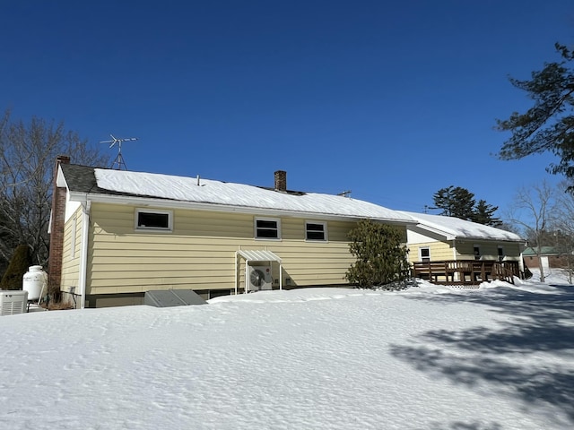 snow covered rear of property with a chimney and a wooden deck