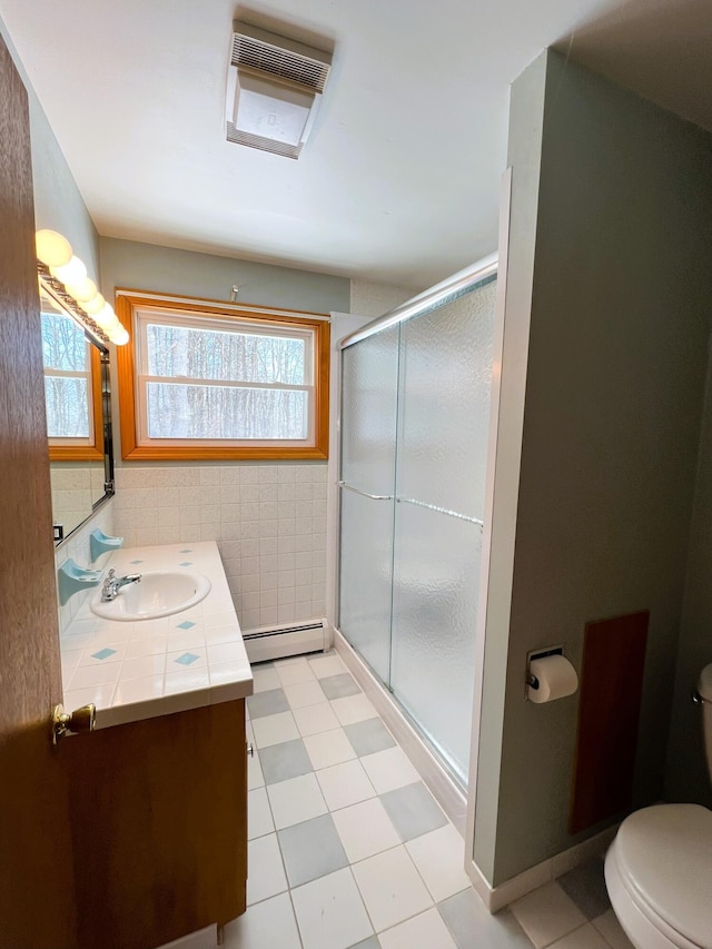 full bathroom with tile walls, toilet, baseboard heating, a stall shower, and vanity