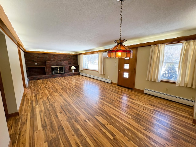 unfurnished living room with a brick fireplace, a textured ceiling, baseboard heating, and wood finished floors