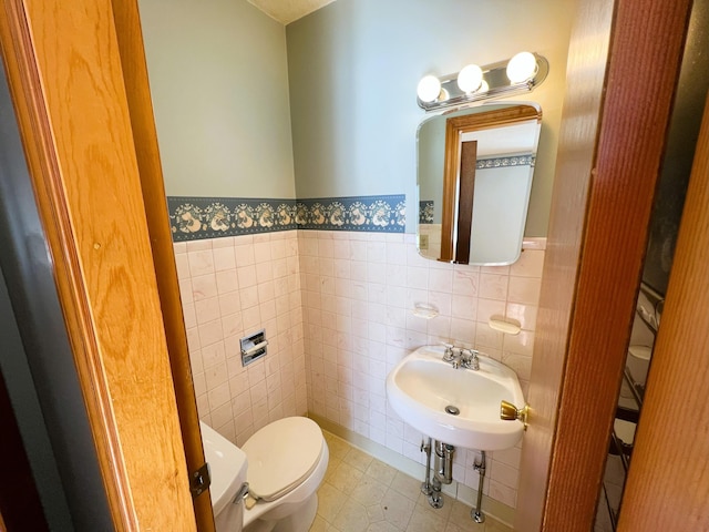 bathroom with a wainscoted wall, tile walls, toilet, a sink, and tile patterned flooring