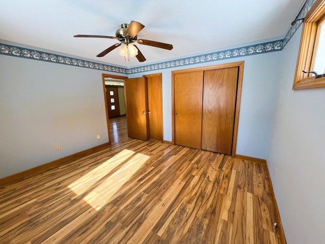 unfurnished bedroom with multiple closets, ceiling fan, baseboards, and wood finished floors