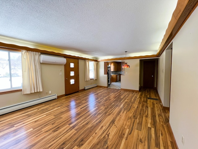 unfurnished living room with an AC wall unit, a textured ceiling, baseboard heating, and wood finished floors