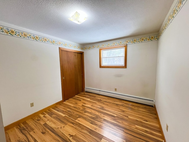 unfurnished bedroom with a textured ceiling, a closet, baseboard heating, and wood finished floors