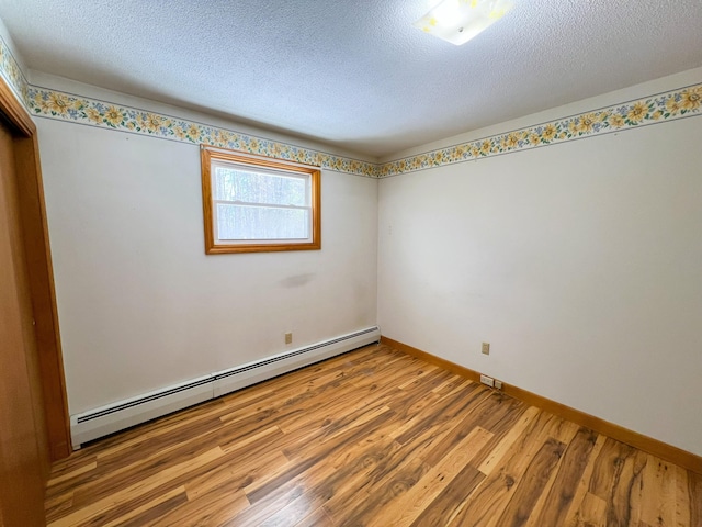 spare room with a textured ceiling, baseboard heating, wood finished floors, and baseboards