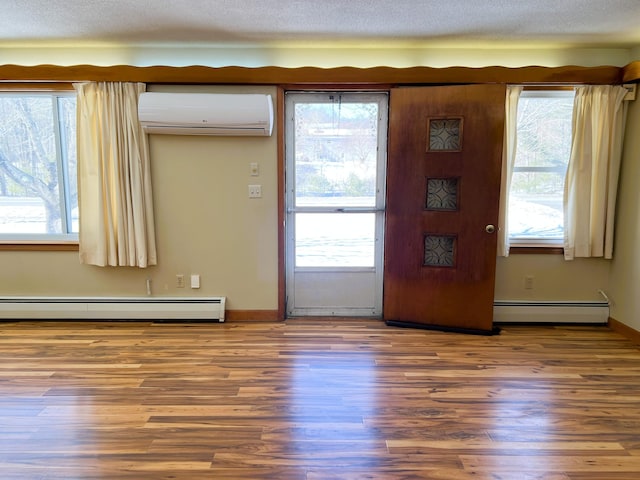 doorway to outside featuring plenty of natural light, a wall mounted AC, a baseboard radiator, and wood finished floors