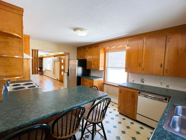 kitchen with white dishwasher, a baseboard heating unit, light floors, stainless steel fridge, and wallpapered walls