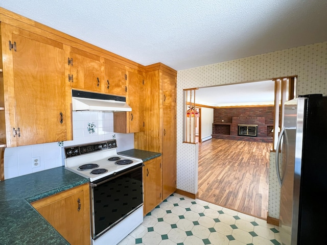 kitchen with wallpapered walls, white range with electric stovetop, light floors, freestanding refrigerator, and under cabinet range hood