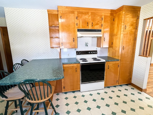 kitchen featuring under cabinet range hood, electric stove, light floors, dark countertops, and wallpapered walls