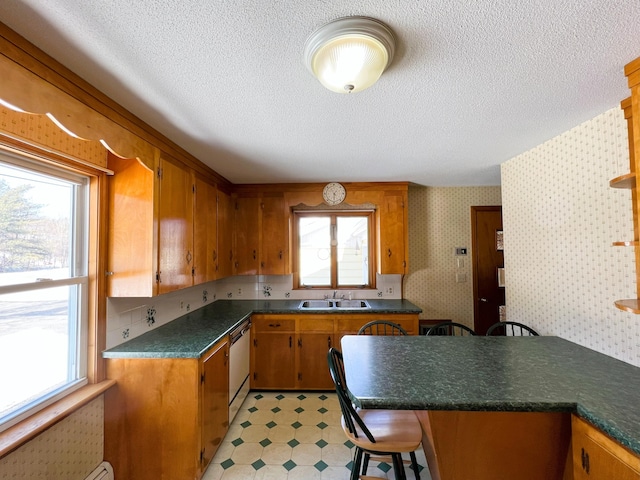 kitchen featuring wallpapered walls, brown cabinetry, dishwashing machine, light floors, and a sink