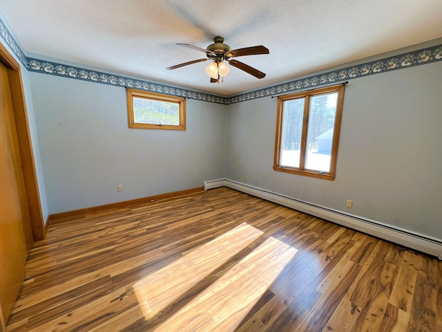 empty room with a baseboard heating unit, a textured ceiling, baseboards, and wood finished floors