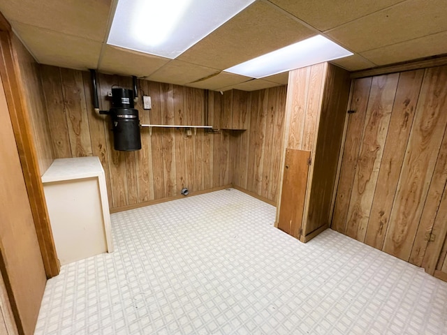 finished basement with wooden walls, a drop ceiling, and tile patterned floors