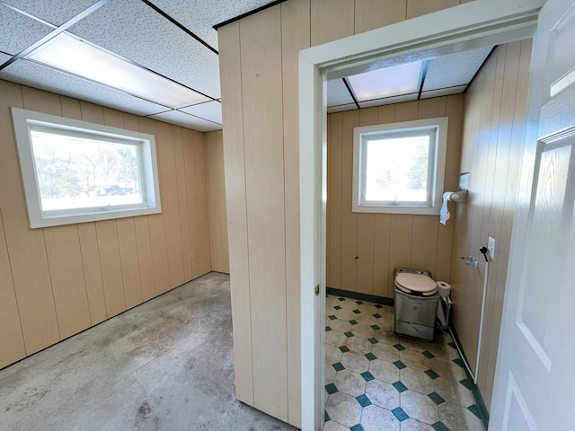 bathroom featuring a healthy amount of sunlight, wood walls, and a paneled ceiling