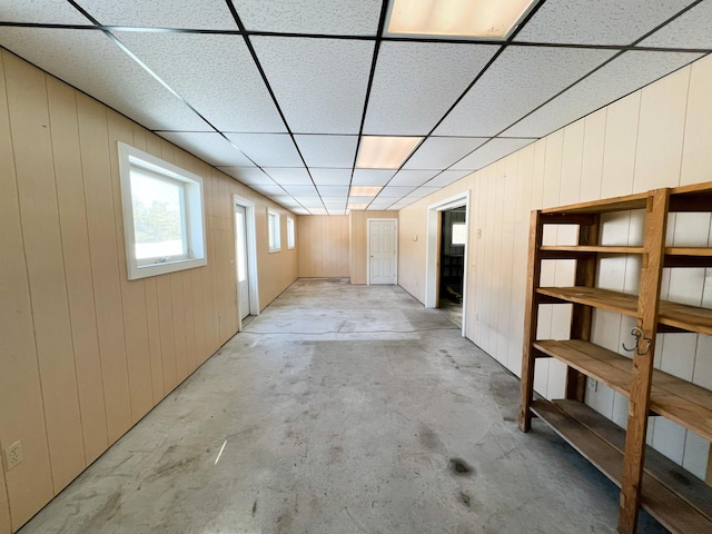 unfurnished room with wooden walls, a paneled ceiling, and unfinished concrete floors