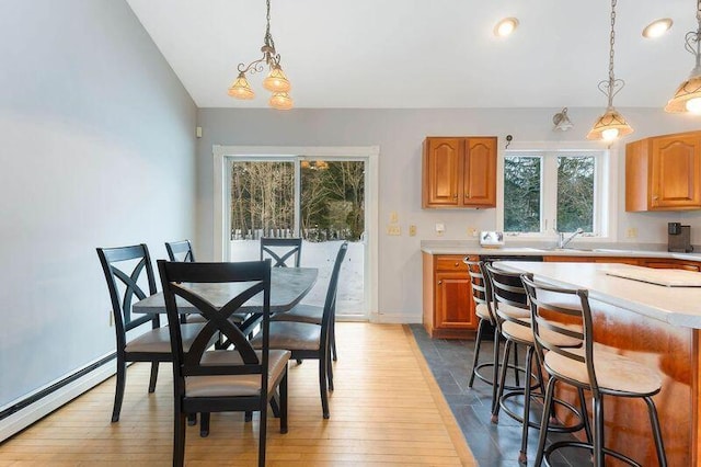 kitchen with lofted ceiling, a breakfast bar, light countertops, baseboard heating, and pendant lighting